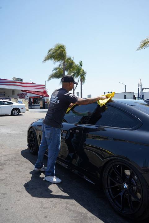 Crew member hand drying a black sedan with a yellow towel