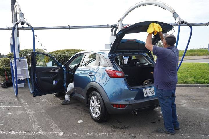 Crew member hand drying a blue Mazda CX-3 with the doors and hatch open