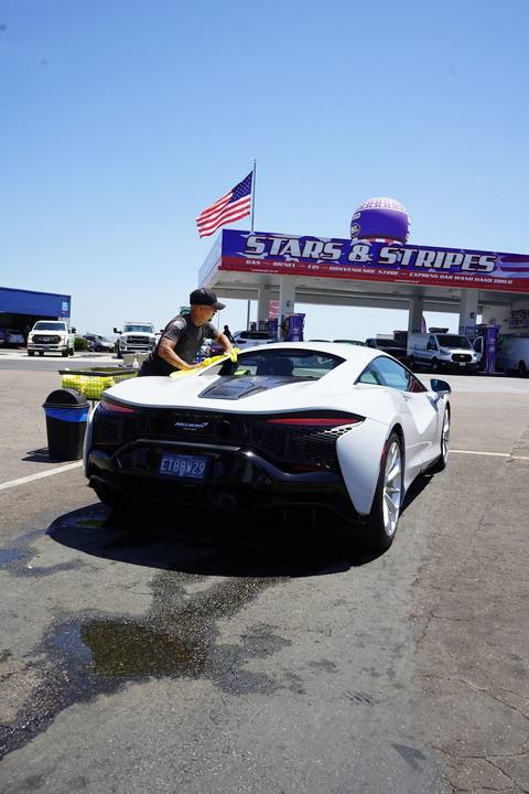 Crew member hand drying a white McLaren Artura under the Stars and Stripes sign and flag