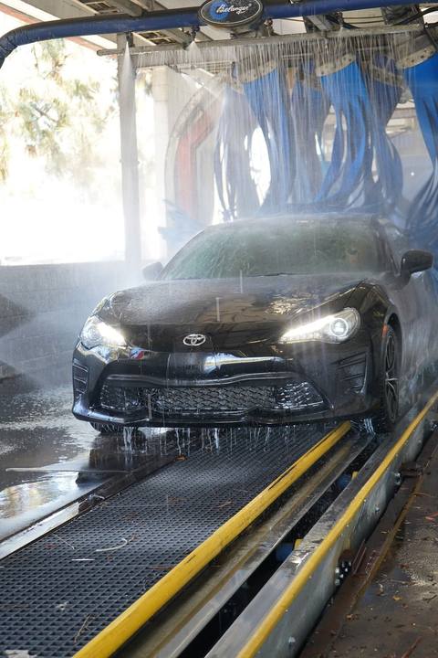 Black Toyota Camry rolling out of the wash tunnel through the mist
