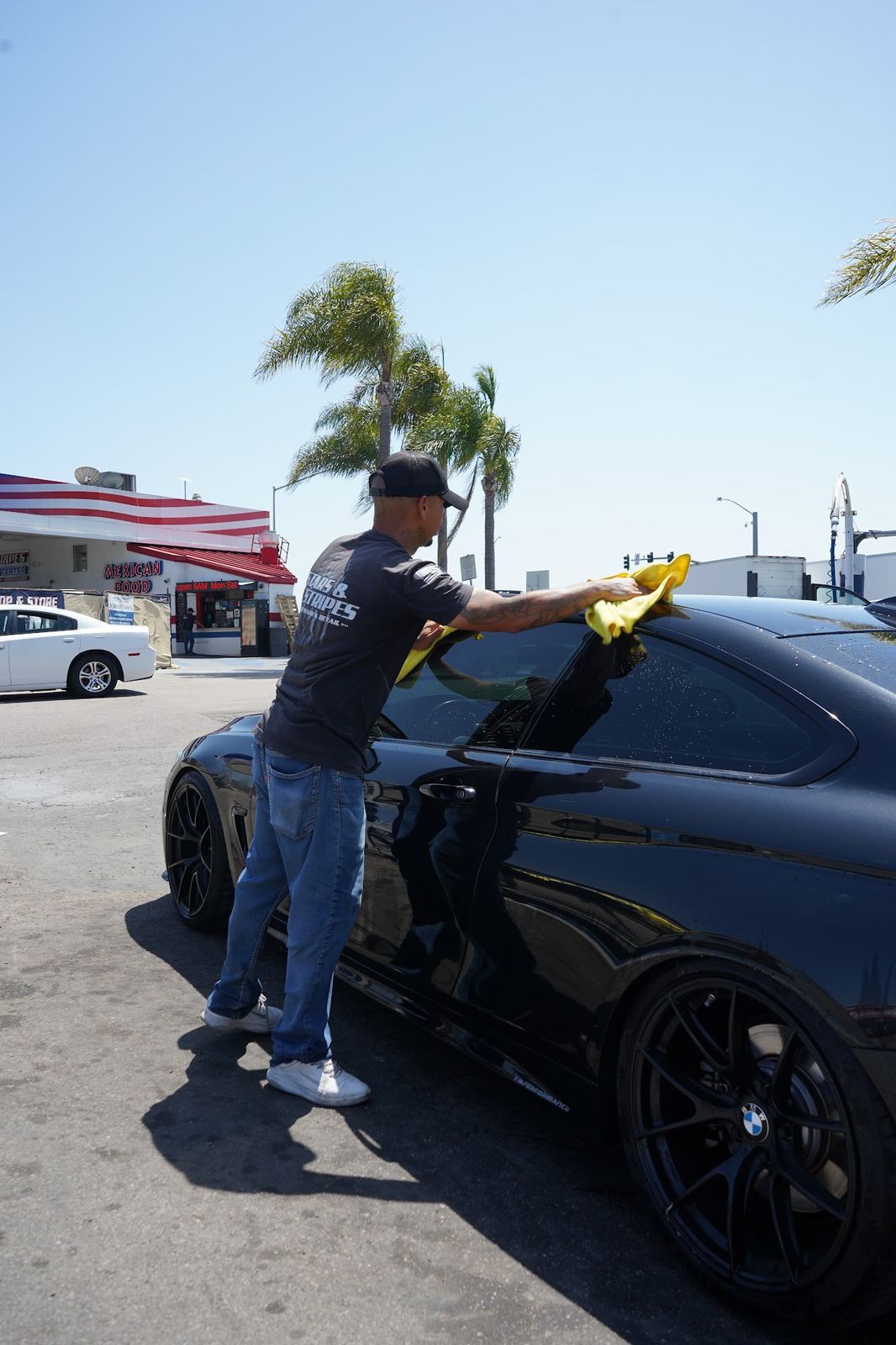 Crew member hand drying a black sedan with a yellow towel