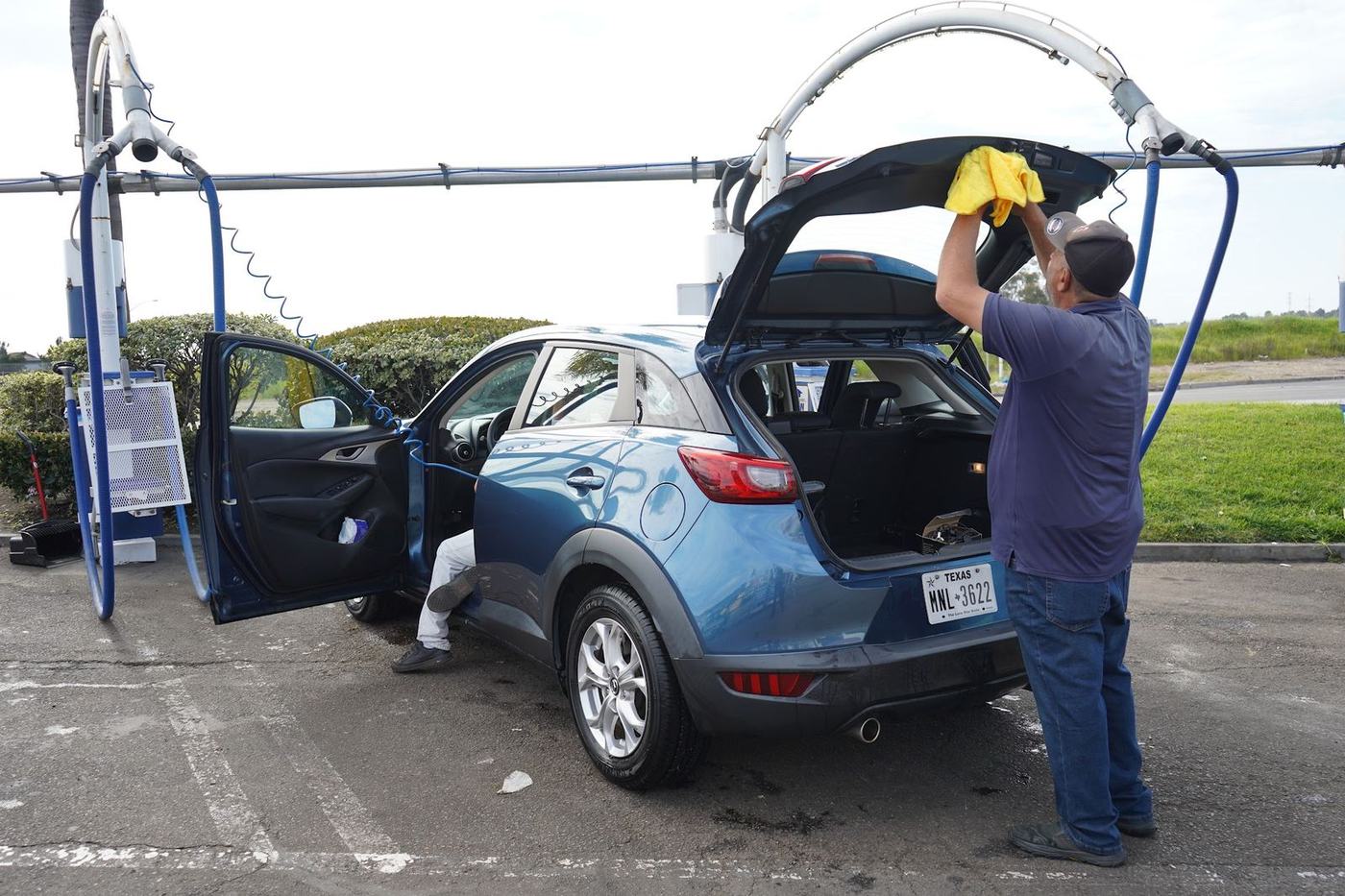 Crew member hand drying a blue Mazda CX-3 with the doors and hatch open