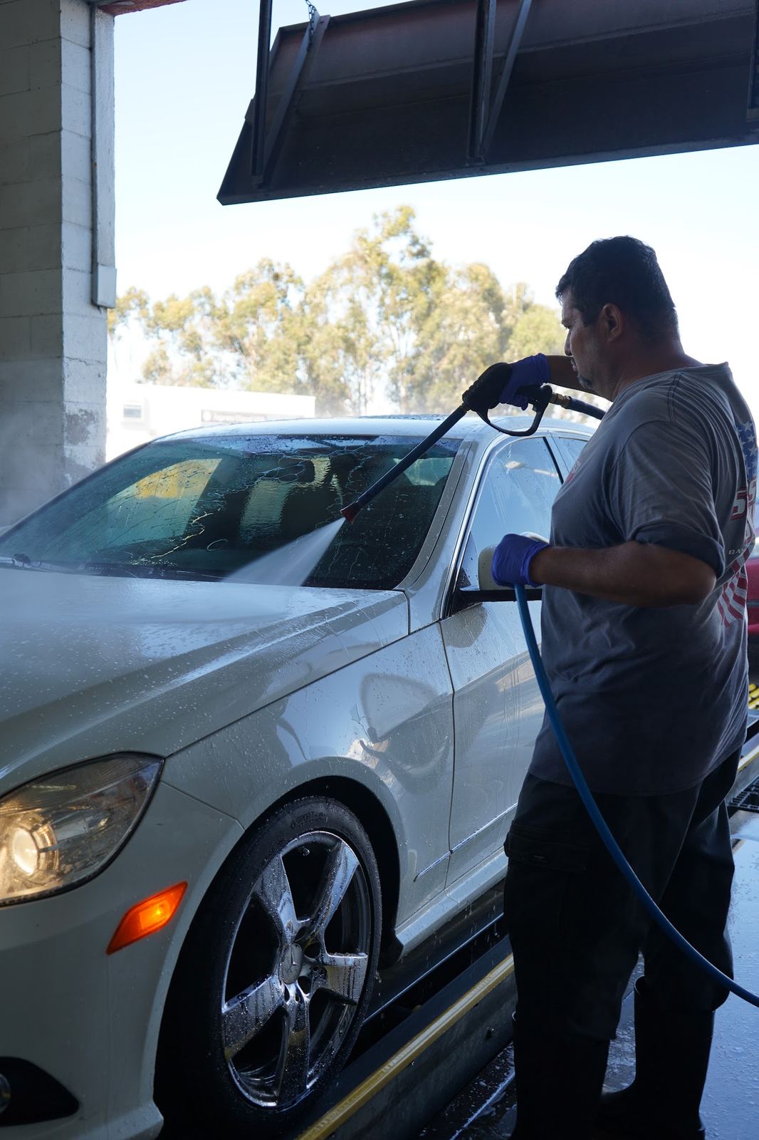 Crew member pressure rinsing a white Mercedes E-Class