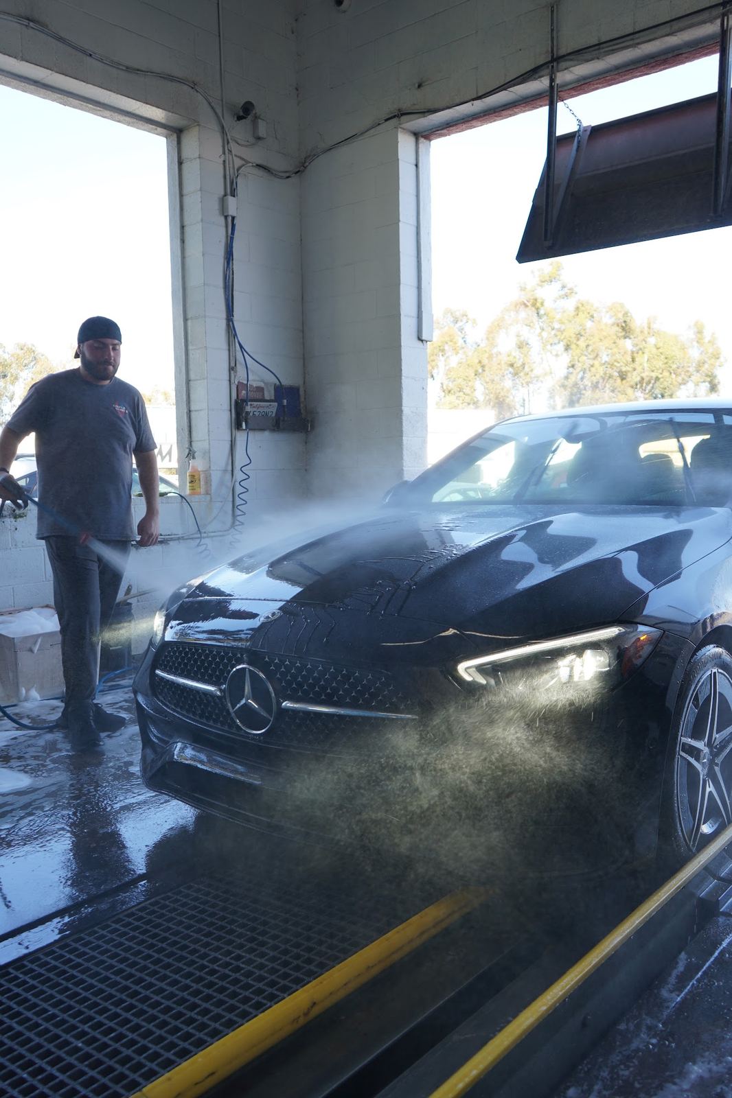 Crew member pre-rinsing a black Mercedes C-Class at the tunnel entrance